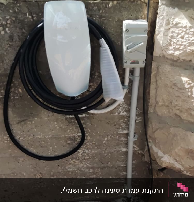 מטען לרכב חשמלי עם כבל שחור על קיר אבן